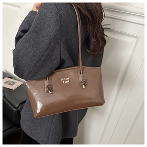 Brown glossy leather tote bag shown on model highlighting size and knotted strap detail
