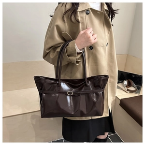 Detail of dark brown glossy tote bag with metal buckle strap and long shoulder straps