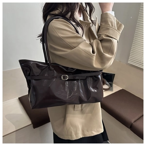 Detail of dark brown glossy shoulder bag featuring a sleek metal buckle and long handles