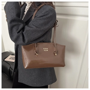 Detail of glossy brown leather shoulder bag featuring gold logo and knot strap accents