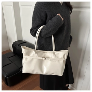 Detail of creamy white patent leather tote bag with metallic buckle strap and glossy finish