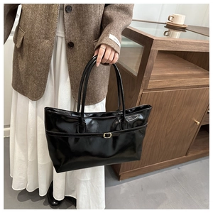 Detail of a black glossy bucket bag with golden buckle on a vintage blazer outfit