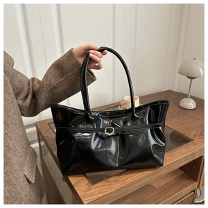 Close-up of glossy black shoulder bag with metal buckle on a minimalist office desk
