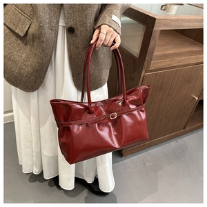 Macro view of dark red glossy patent leather tote bag with elegant gold buckle strap detail