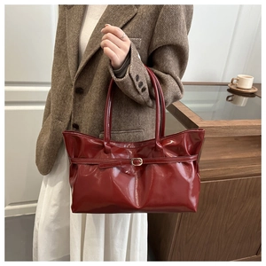 Close-up of a burgundy glossy leather tote bag with a metal buckle on a brown suit outfit