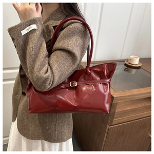 Deep red patent leather underarm bag with decorative belt buckle shown on shoulder