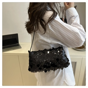 Detail of black sequined underarm bag with slim strap shown on striped shirt