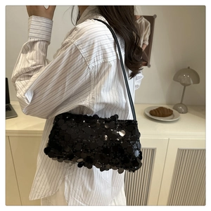 Detail of shimmering black sequins and sleek shoulder strap on a party baguette bag