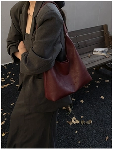 Detail of burgundy leather tote bag with grainy texture and logo in autumn park setting