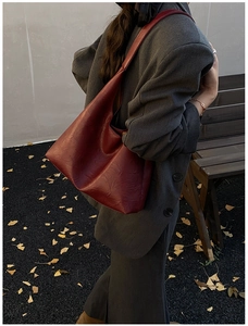 Close-up of a burgundy large leather tote bag worn by a model in an autumn setting
