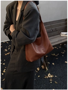Outdoor shot of a textured caramel leather tote bag styled with a grey suit and autumn leaves