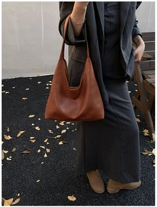 Close-up of caramel brown shoulder bag with embossed fashion logo and wide strap detail