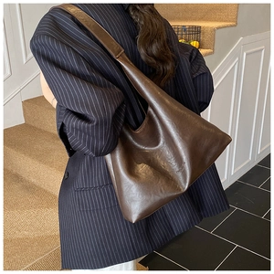 Detail view of large dark brown leather tote bag worn as a vintage style shoulder bag
