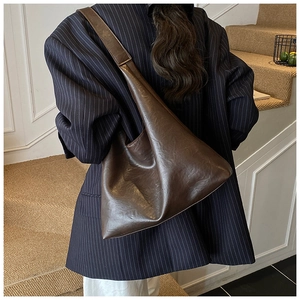 Deep brown retro hobo bag shown over the shoulder of a model in a navy pinstripe suit