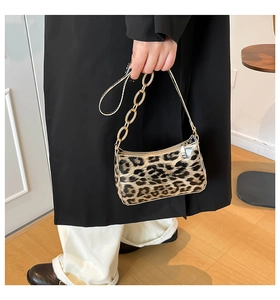 Detail of leopard print handbag with glossy gold chain strap on minimalist background