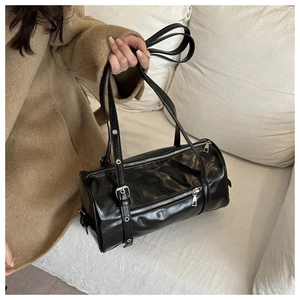 Fashionable black glossy pillow bag shown on a sofa, featuring stylish silver zippers