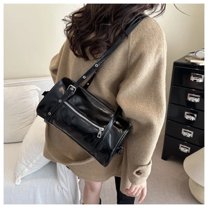 Side view of black glossy leather Boston bag with silver eyelet adjustable strap