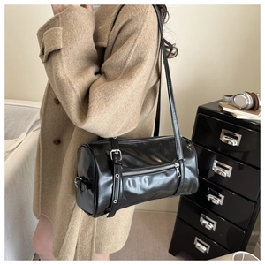 Detail view of a black glossy leather cylinder shoulder bag with silver buckle and zippers