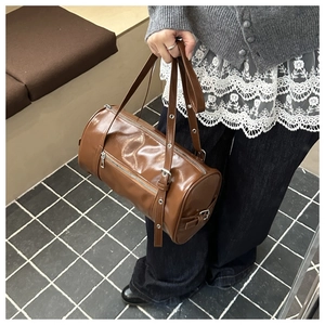 Detail of a brown cylindrical pillow bag with silver zippers and adjustable straps