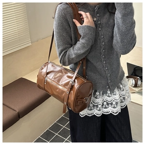 Close-up of brown vintage leather cylinder bag with silver buckles and eyelet details