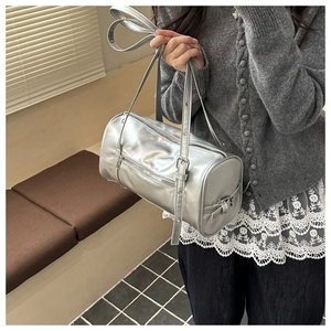 Detail of silver cylindrical pillow bag showing high-gloss PU texture and zipper on model