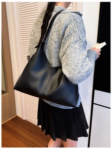 Detail of minimalist black large capacity tote bag worn over the shoulder by model