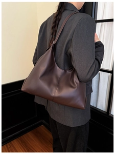 Detail view of large dark brown leather tote bag worn as an underarm shoulder bag