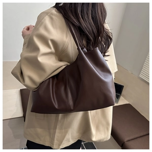 Detail of soft dark brown leather tote bag with wide strap on model's shoulder