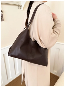Dark brown large capacity tote bag worn with a beige coat in a minimalist home setting