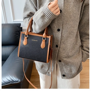 Detail of a chic black textured leather tote with brown handles and golden fashion text