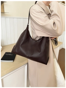 Detail of a dark brown large PU leather crescent tote bag on a model in a beige coat