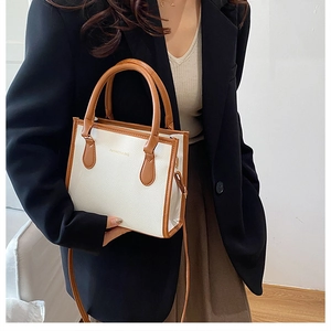 Detailed close-up of a white lychee grain crossbody bag with brown trim and gold text