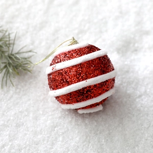 Sparkling red Christmas ball with white spiral glitter and gold string on snow background