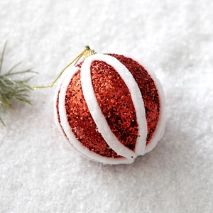 Detail of red glitter Christmas ball with white flocked stripes on snowy background