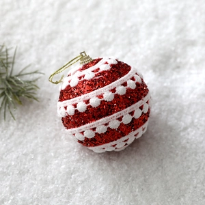 Detail of red glitter Christmas ball with white lace trim and gold string on snow