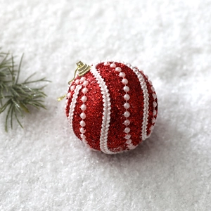 Detail of red Christmas ball with white glitter waves and pearls on snowy background