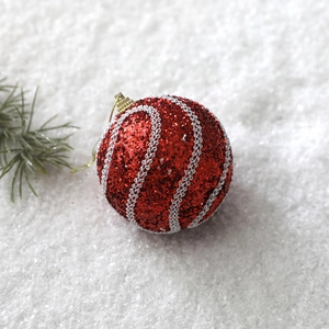 Detail of an 8cm red glitter Christmas ball with white braided patterns and gold hanger
