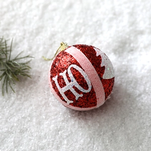 Close-up of red glitter Christmas ball with white HO slogan on snowy pine branch