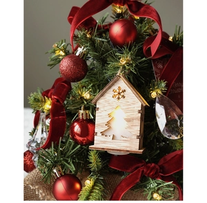 Close-up of artificial Christmas tree with glowing wooden house and red velvet bows