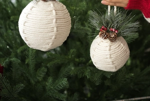 Detail of handmade white cotton rope Christmas ball ornaments with pine and berries