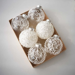 Detail of 6pcs clear Christmas ornaments with white lace and snowflake patterns in a box