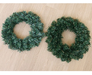 Detailed view of two plain green artificial PVC pine wreaths on light wood background