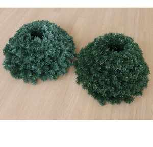 Detail view of two dense green artificial pine needle wreaths on light wood floor