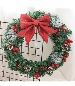 Détail de couronne de Noël avec nœud rouge pailleté, pommes de pin et baies sur sapin