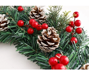 Détail d'une couronne de Noël avec pommes de pin enneigées, baies rouges et épines de pin