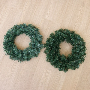 Set of two green artificial pine Christmas wreaths on light wood floor for holiday decor