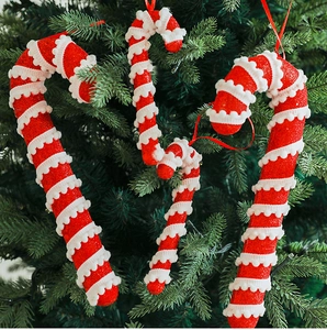 Detail of glittery red and white candy cane ornaments hanging on a green Christmas tree
