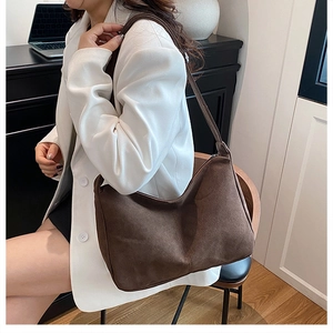 Detail view of large dark brown suede tote bag with stylish half-moon shape on model