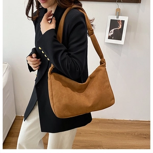 Détail du sac hobo en daim marron avec bandoulière réglable porté sur un blazer