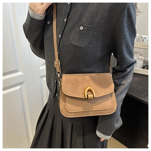 Detail of vintage crossbody bag featuring suede textures and a gold horseshoe buckle